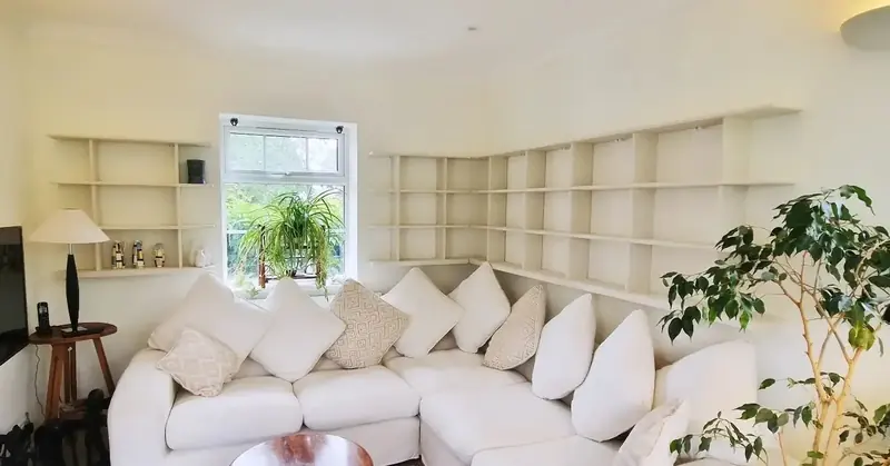 Cream shelves running around a curved living room wall behind a large corner sofa
