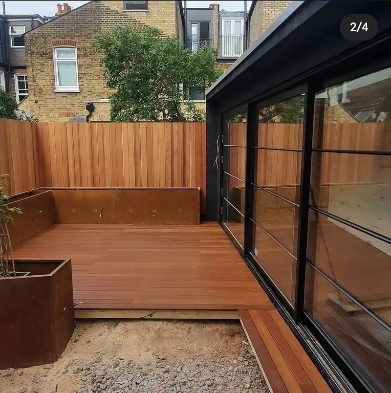 Red hardwood decking with a raised planter beside black-framed glass doors