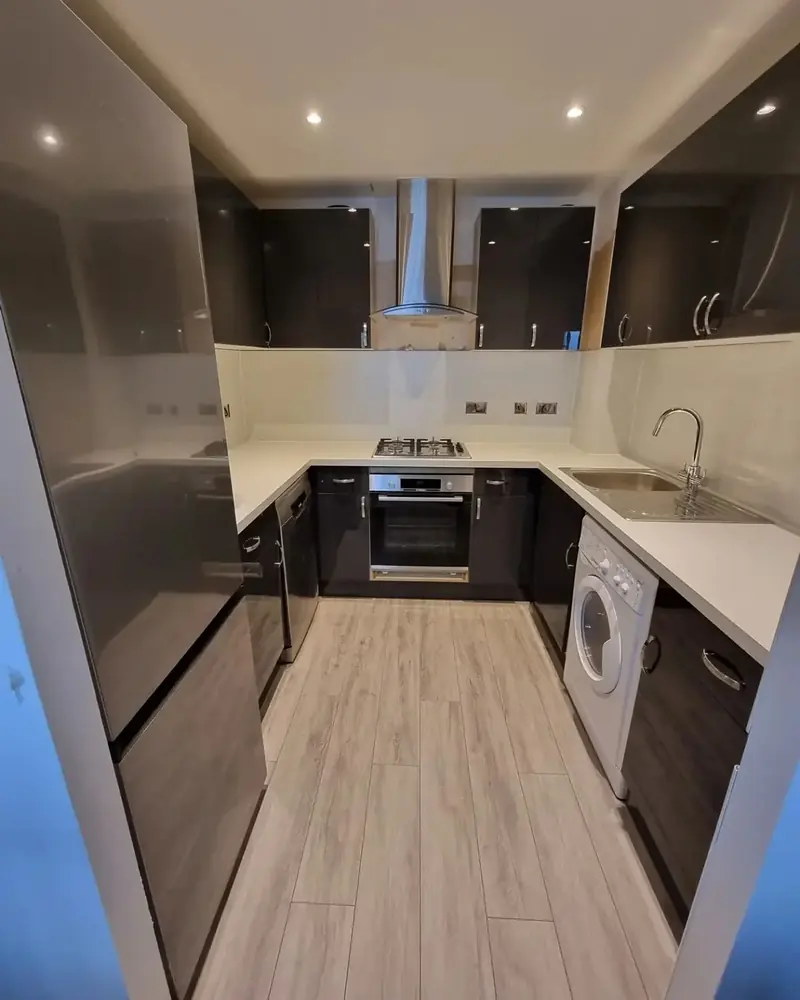 Galley kitchen with dark grey cabinets, white worktops, built-in oven and wood-effect floor