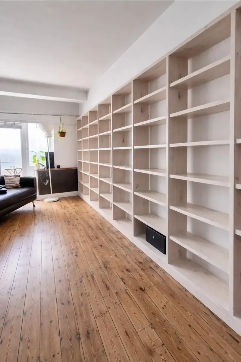Long run of floor-to-ceiling white bookshelves over a dark oak floor