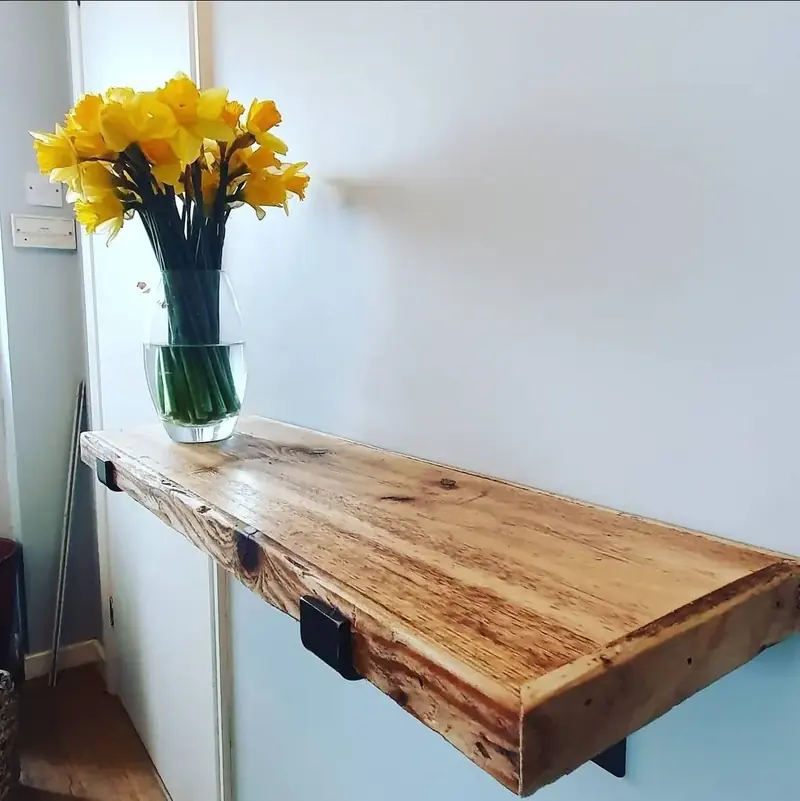 Thick live-edge timber shelf floating on a white wall with a vase of daffodils
