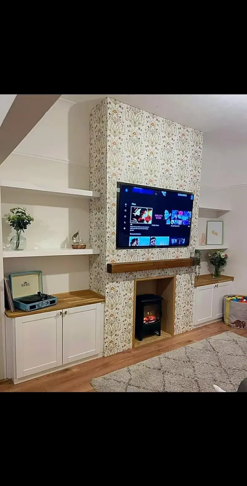 Chimney breast with patterned tiles, a TV and log burner, framed by white alcove cupboards and shelves