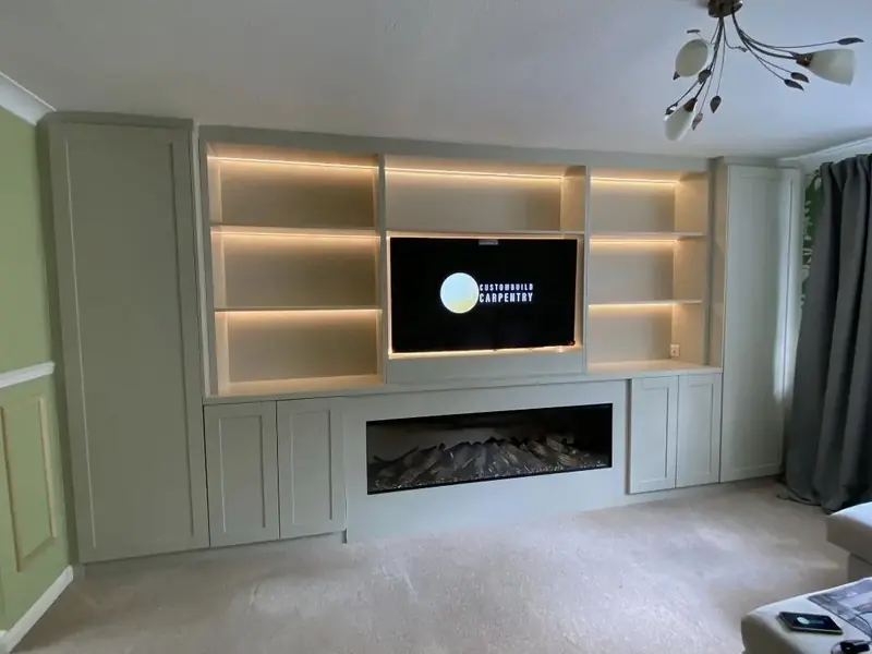 Built-in media wall with lit alcove shelves either side of a wall-mounted TV and a long inset electric fire