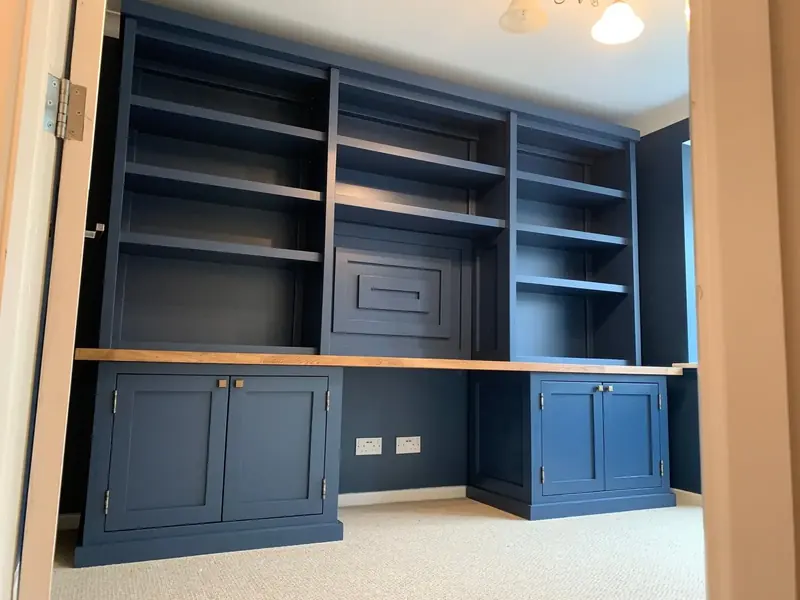 Navy blue fitted home office with a built-in desk between cupboards and full-width bookshelves above