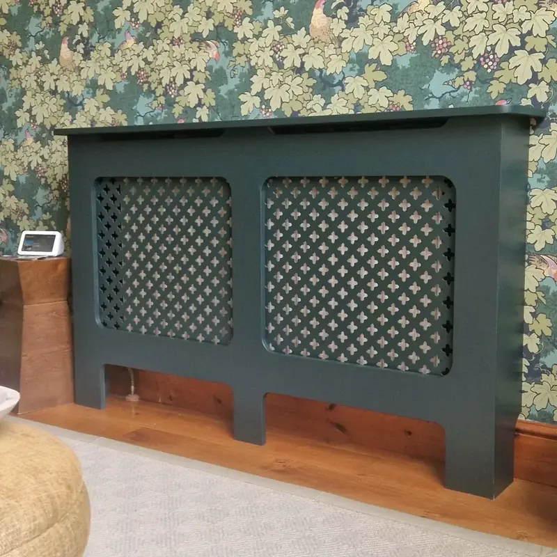 Dark green radiator cover with lattice grille against floral wallpaper