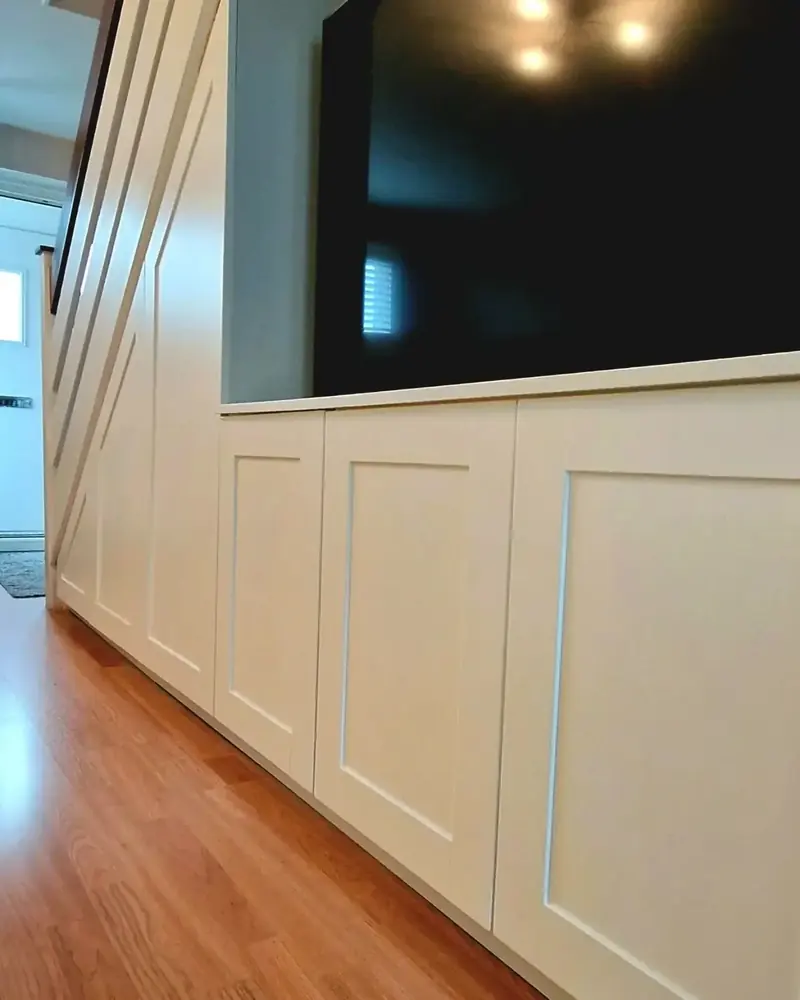 Run of white shaker-style cupboards under stairs with a TV above