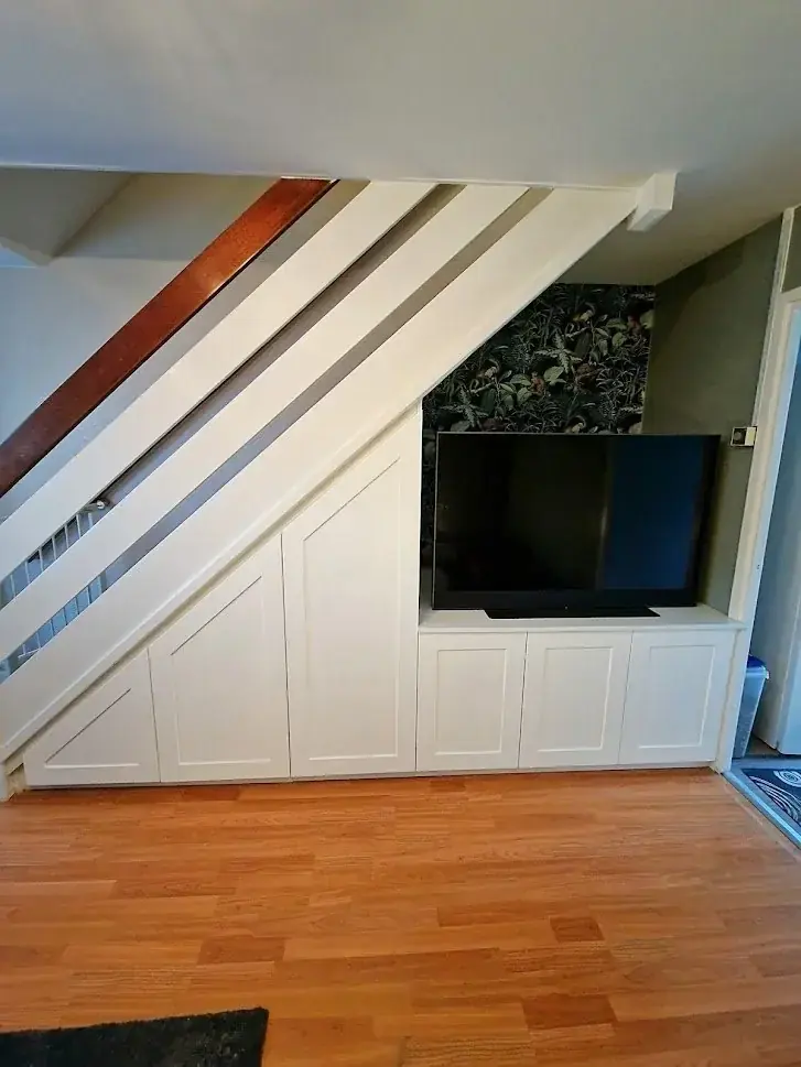 White panelled cupboards built under a staircase with a TV mounted in a recess