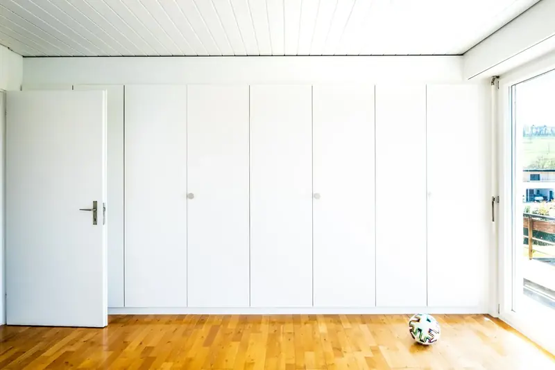 Long run of white flat-fronted fitted wardrobes on a wooden floor